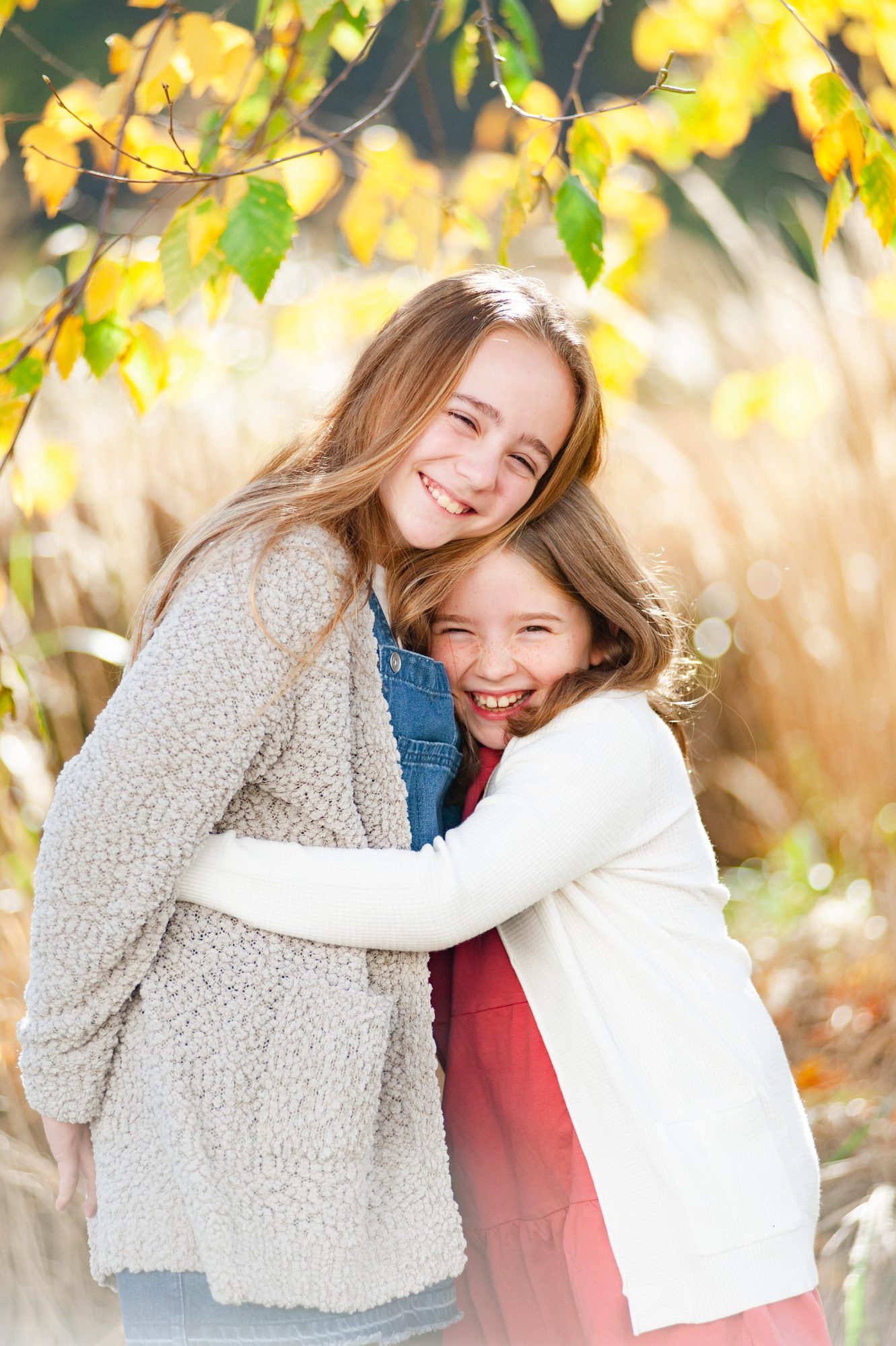 sisters embrace and smile on a sunny day outdoors during a family photo session