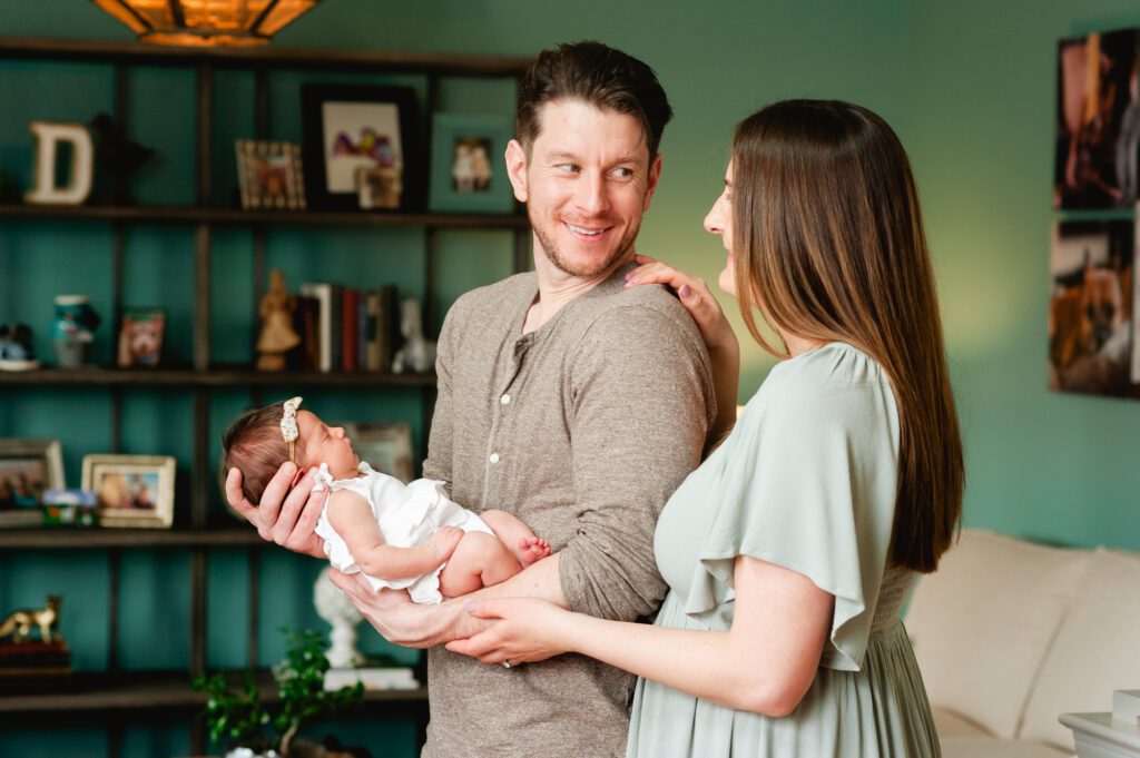 Dad holding newborn baby and smiling at mom who is standing next to him in their home captured by Philadelphia Newborn Photographer