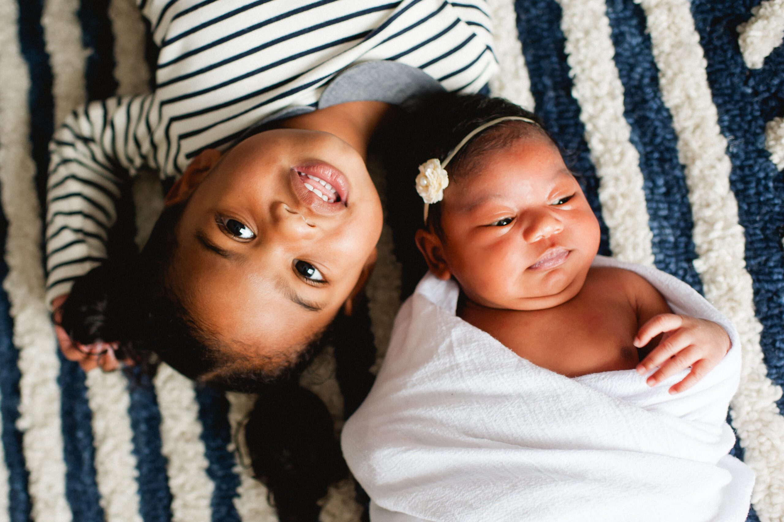 a toddler girl lays upside down next to her newborn sister during a Philadelphia family photo session