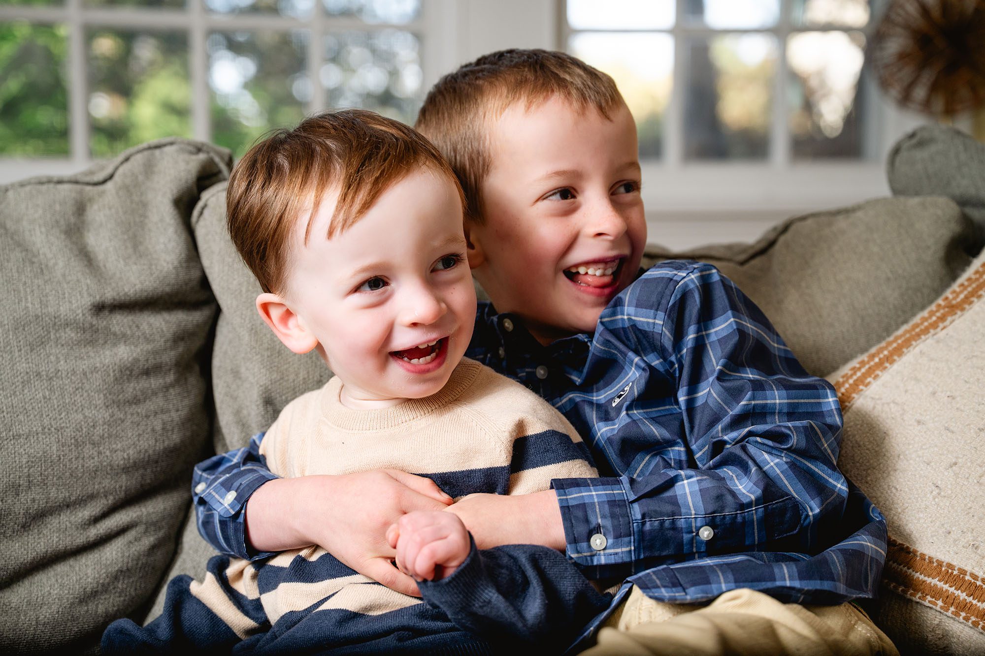 brothers hug and laugh while sitting on their living room couch during a Philadelphia family photo session